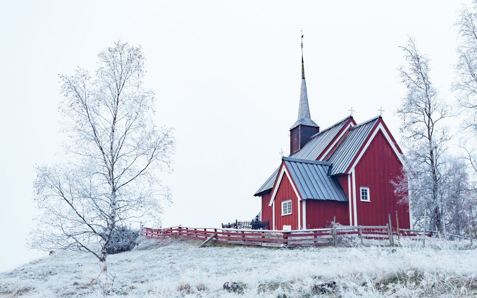 Rött träkapell med spetsigt torn i ett snötäckt landskap med frostiga björkar