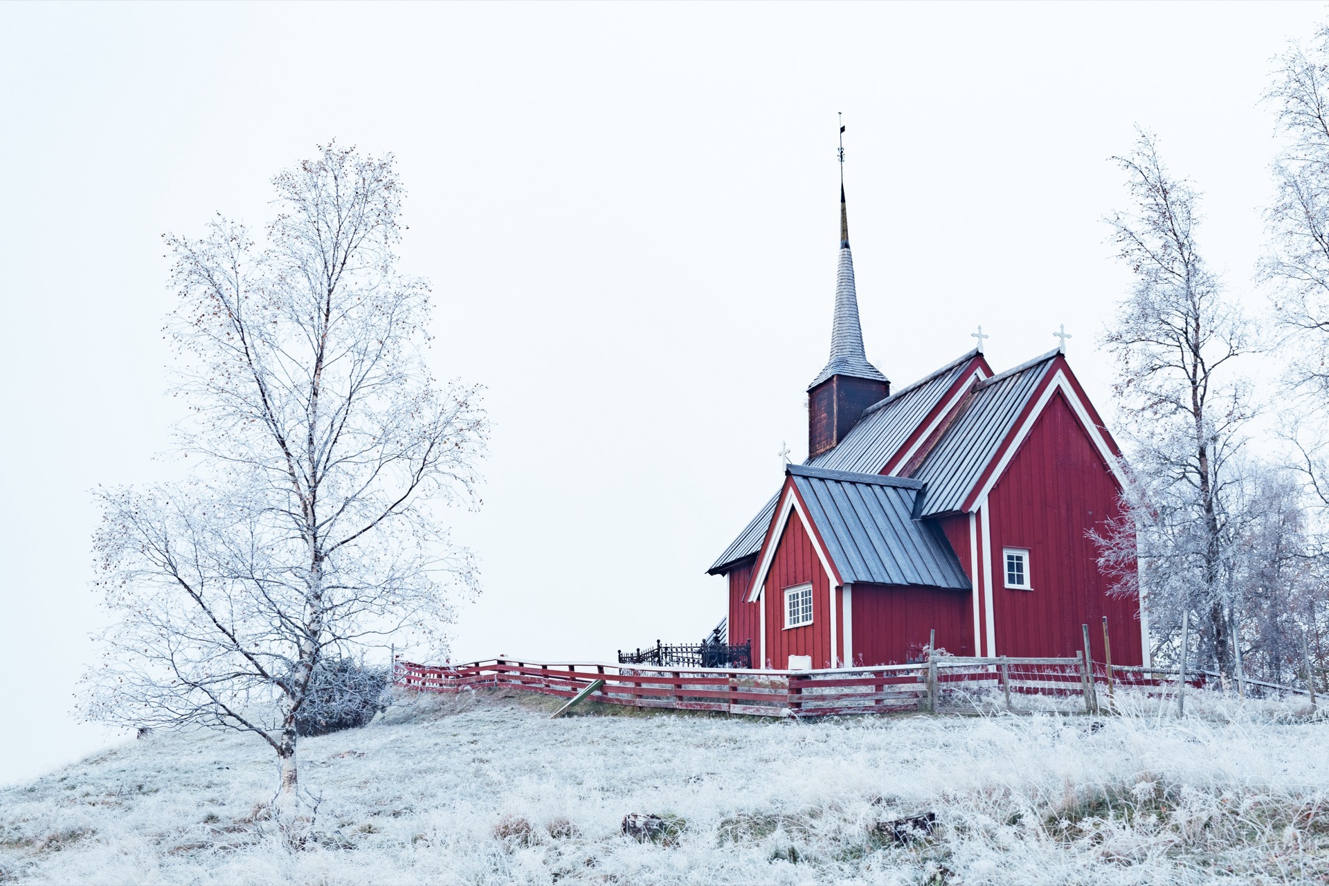 Rött träkapell med spetsigt torn i ett snötäckt landskap med frostiga björkar